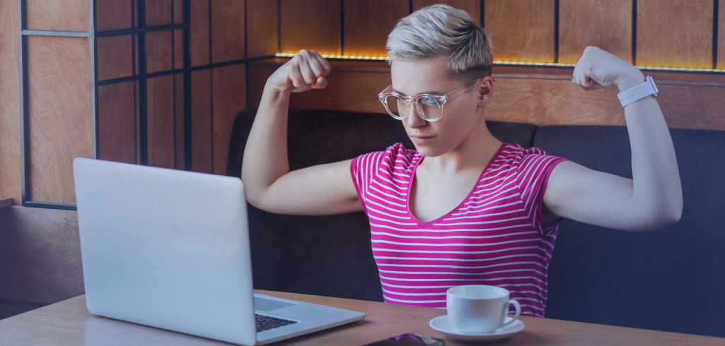 Une femme aux cheveux courts est assise devant son ordinateur de travail. Elle contracte ses biceps.