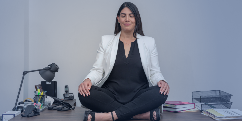 Une femme est assise en tailleur sur son bureau. Elle médite en fermant les yeux.